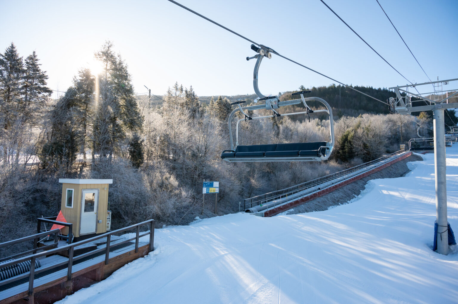 Empty four-person chairlift over a snowy slope at Blue Mountain Resort in the Pennsylvania Poconos, with frost-covered trees and a bright winter sun