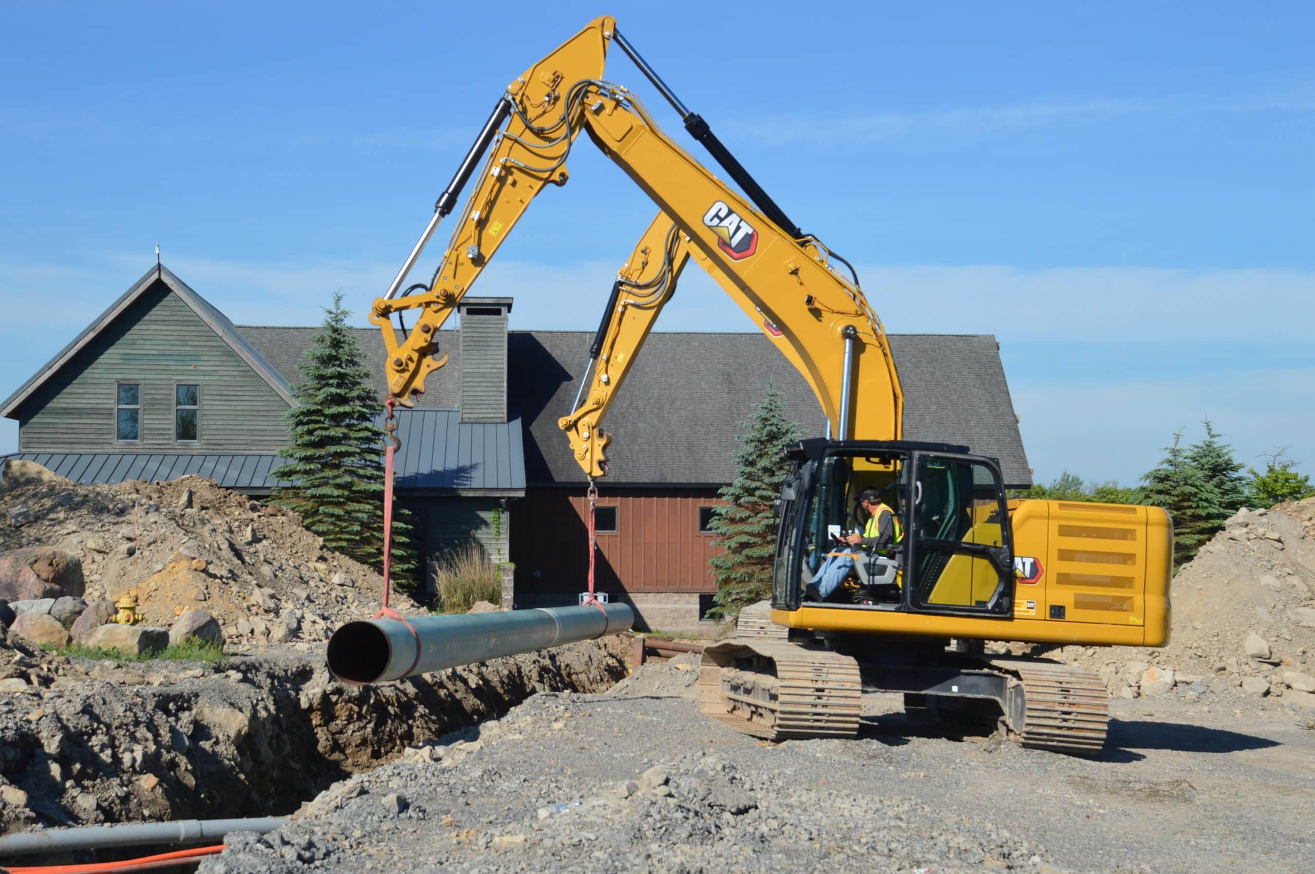 A yellow excavator lifts a section of snowmaking pipeline into a trench at Wisp Resort during summer construction work