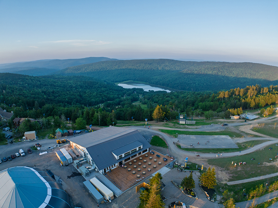 Aerial view of the new Shavers Center at Snowshoe Mountain at dusk, with its deck, the village and Shavers Lake in the valley behind it